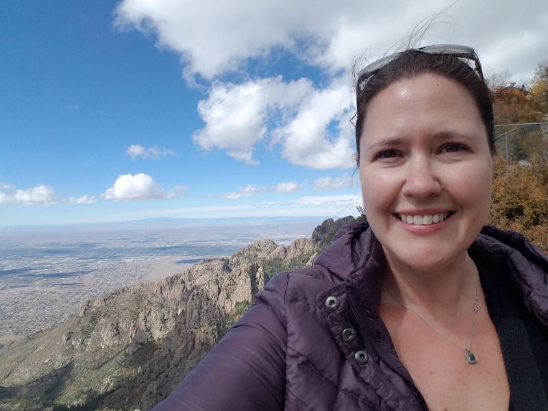 Selfie of woman in purple jacket from the top of Sandia Peak